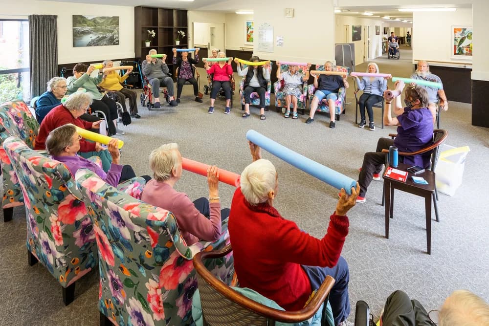 Residents taking part in a seated group exercise session with pool noodles